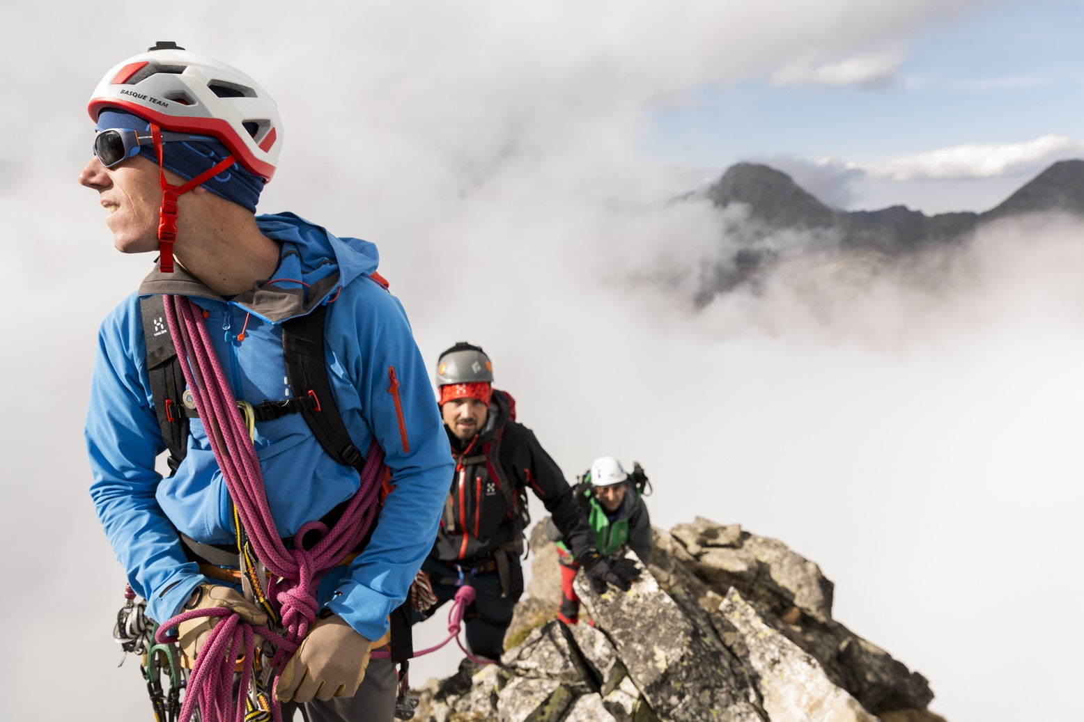 A young man holding a pink climbing rope from which he holds two men in a misty mountain background.